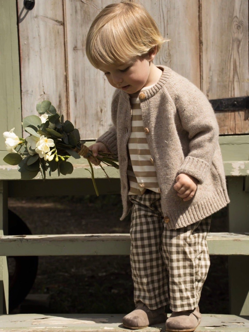 Un niño pequeño con cárdigan tejido, camiseta a rayas y pantalón de cuadros